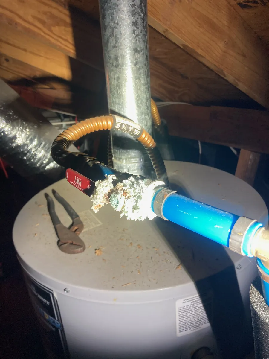The top of a water heater in an attic, with the flue and PEX water lines checked during a phase inspection